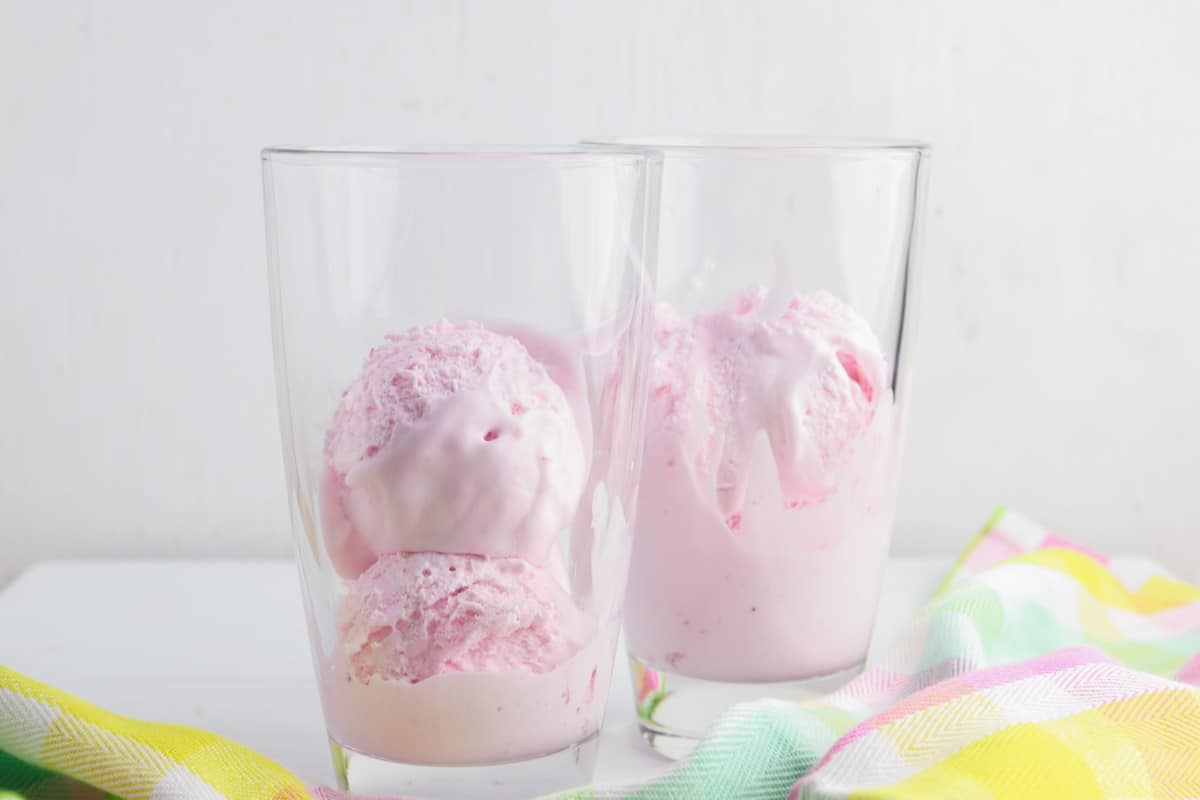 Two drinking glasses each with 2 scoops of strawberry ice cream.