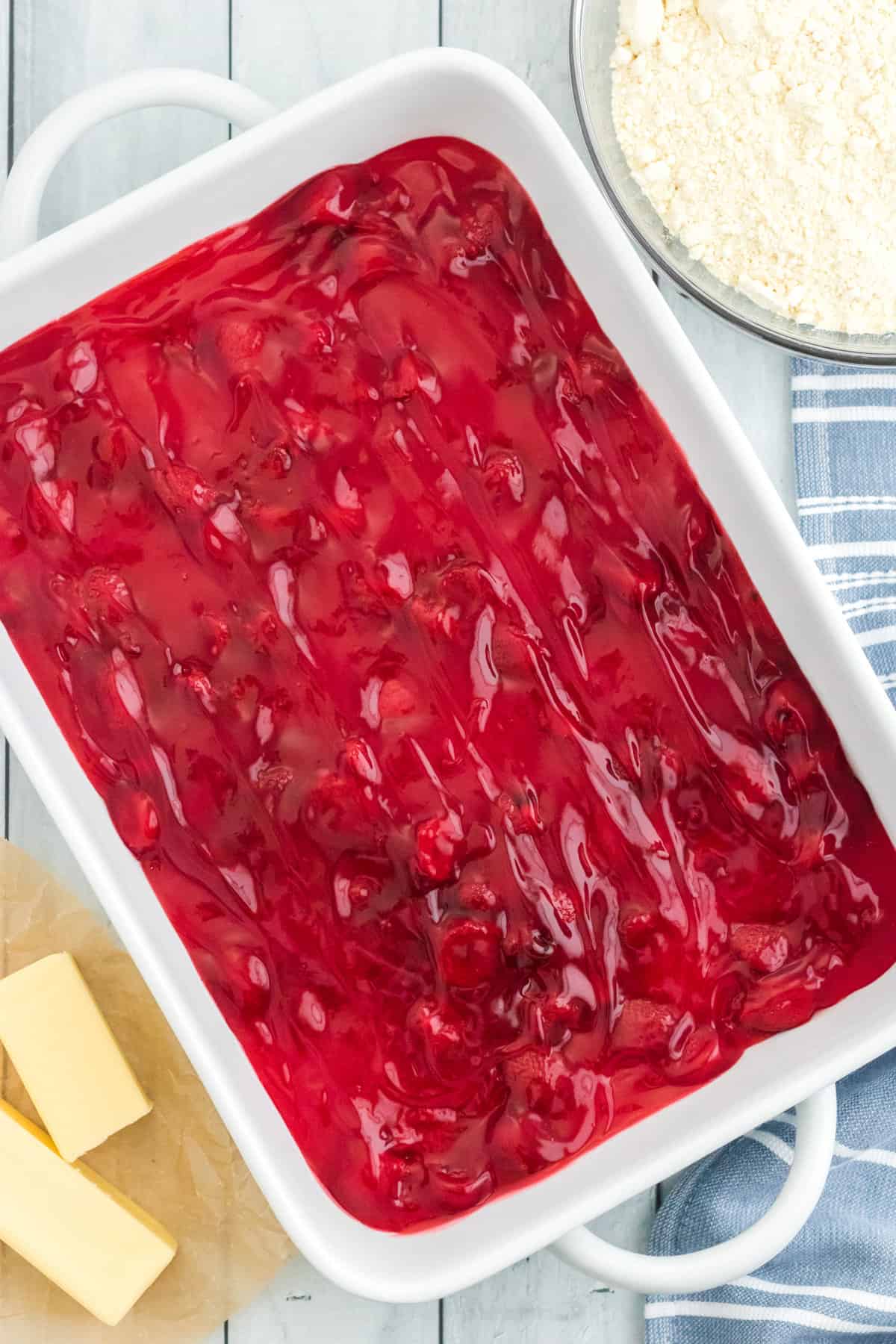 Strawberry pie filling in the bottom of a white 9 x 13 baking dish in an even layer.