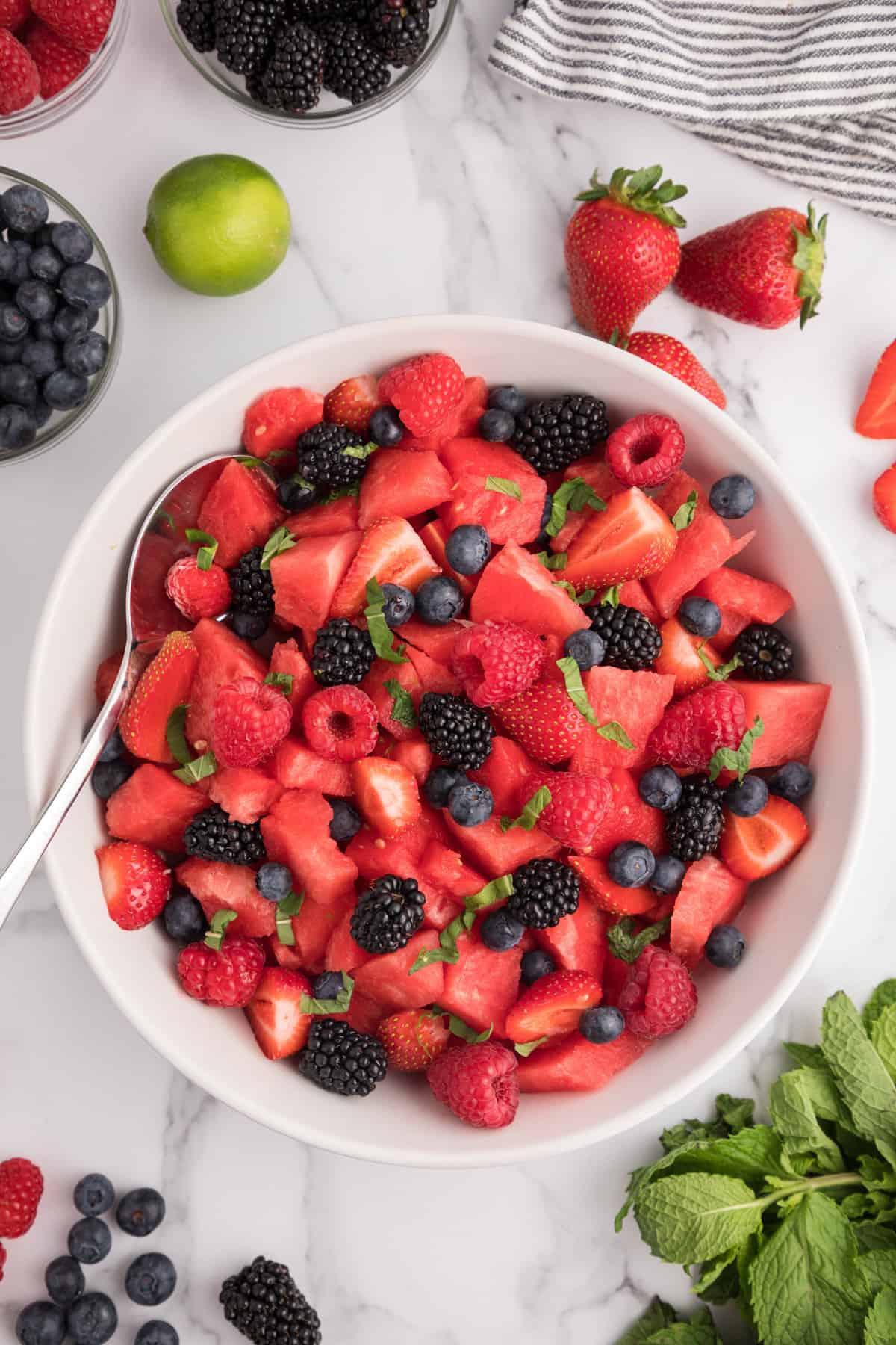 Fresh watermelon and berry salad with serving spoon resting on side of bowl.