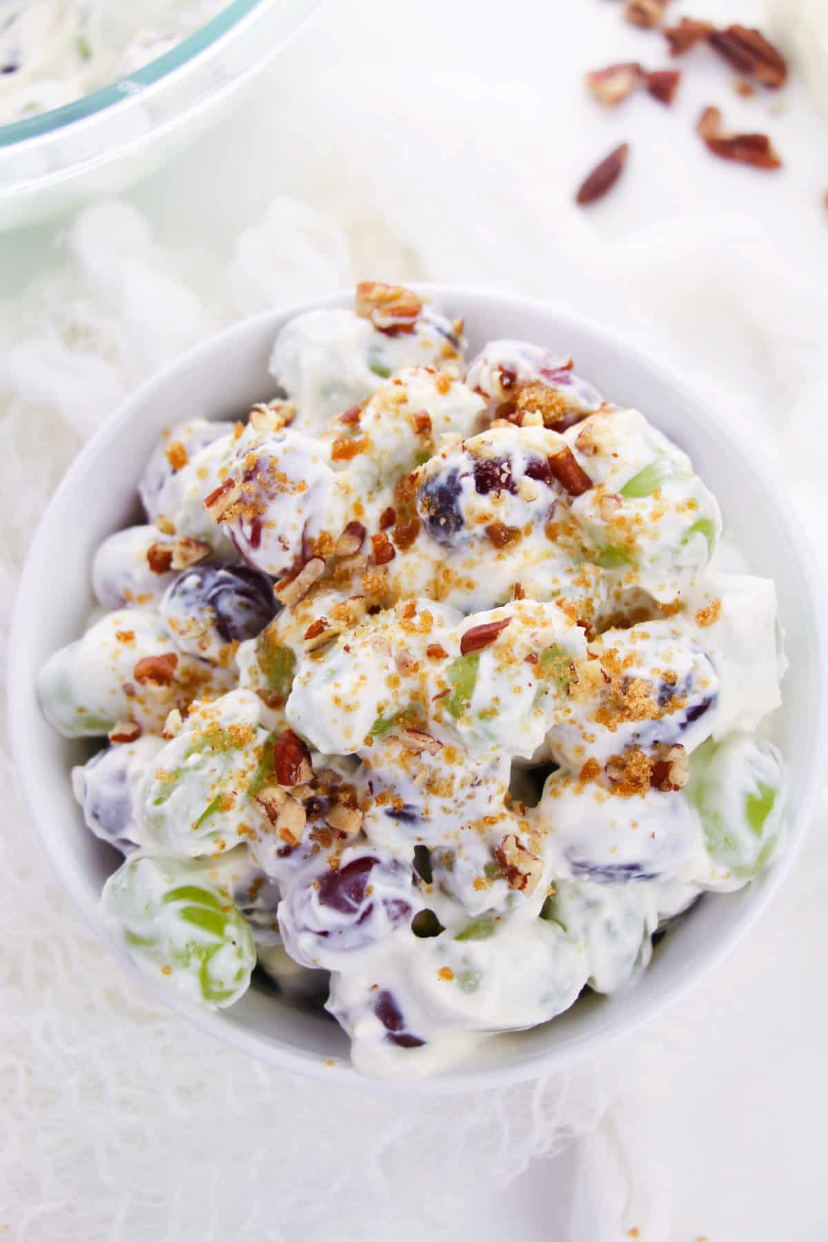 Creamy grape salad white serving bowl topped with pecans.