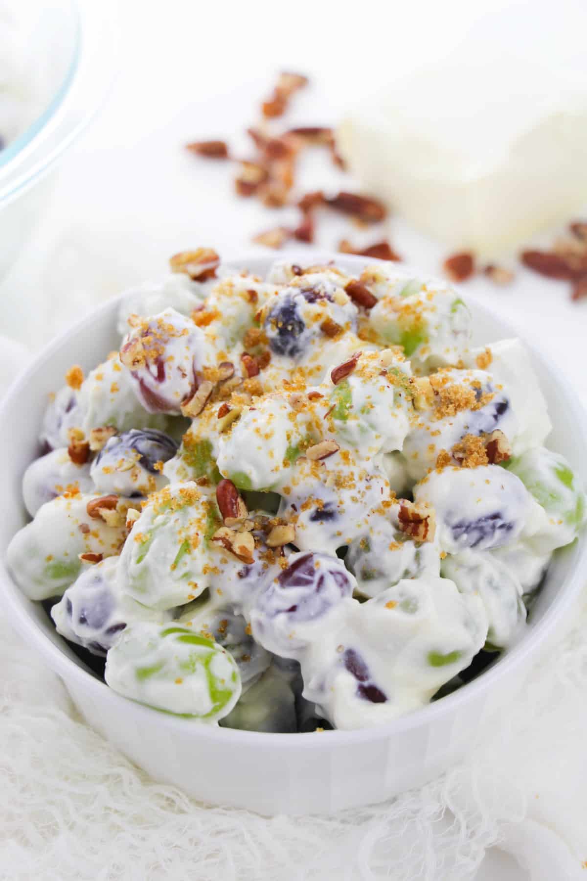 Bowl of grape salad with creamy yogurt dressing topped with crushed pecans and brown sugar.
