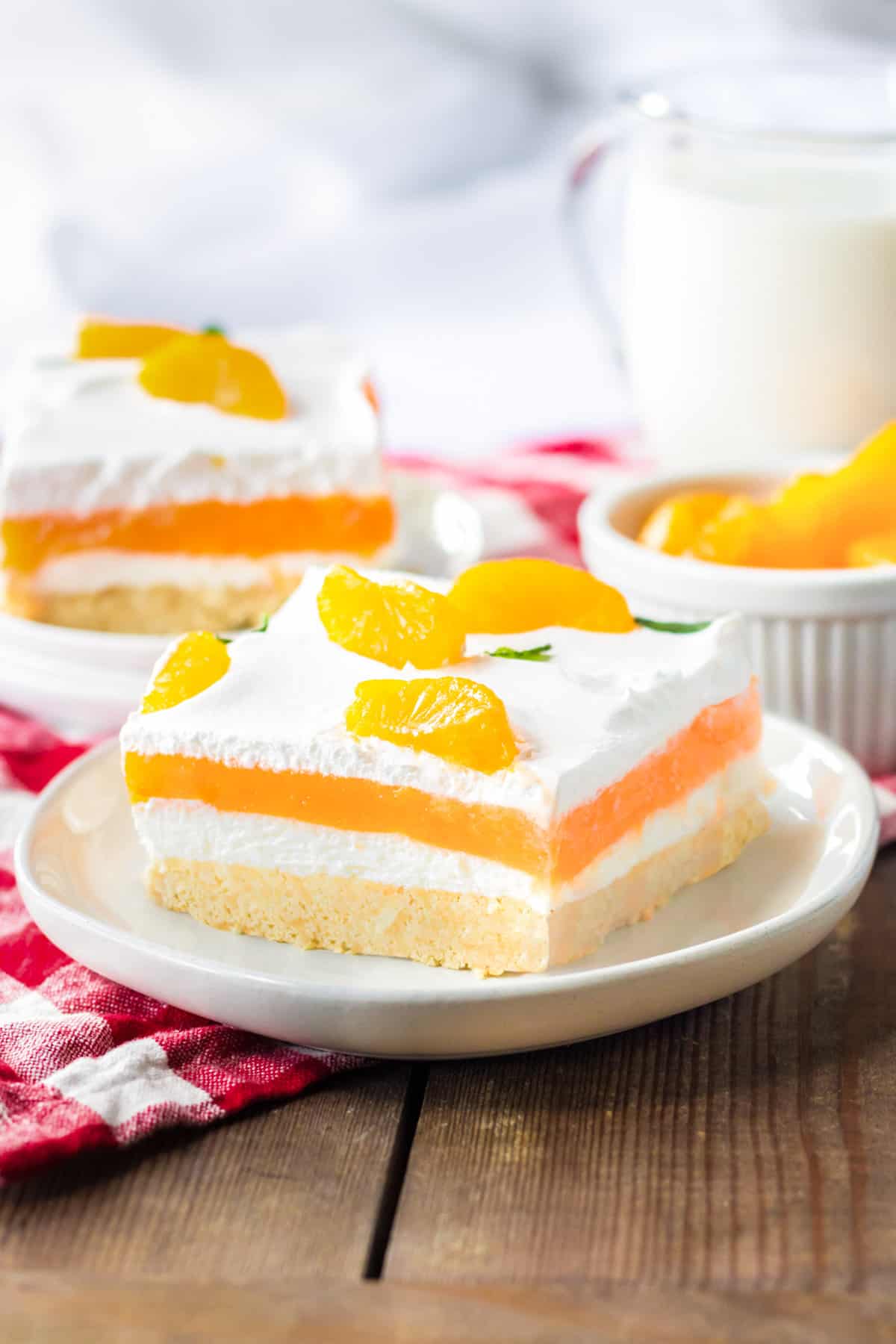 Orange creamsicle lush with layers of creamy vanilla pudding and orange jello, sweetened cream cheese, and cool whip on a sweet cookie crust. Mandarin orange pieces top the no bake cake.