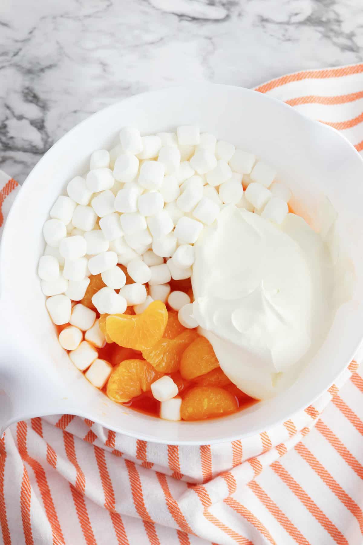 Mandarin oranges, mini marshmallows, and whipped topping added to jello in mixing bowl.