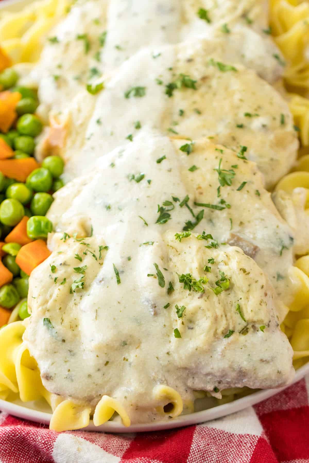 Creamy oven baked pork chops with cream of mushroom sauce and parsley garnish served with noodles and mixed vegetables.