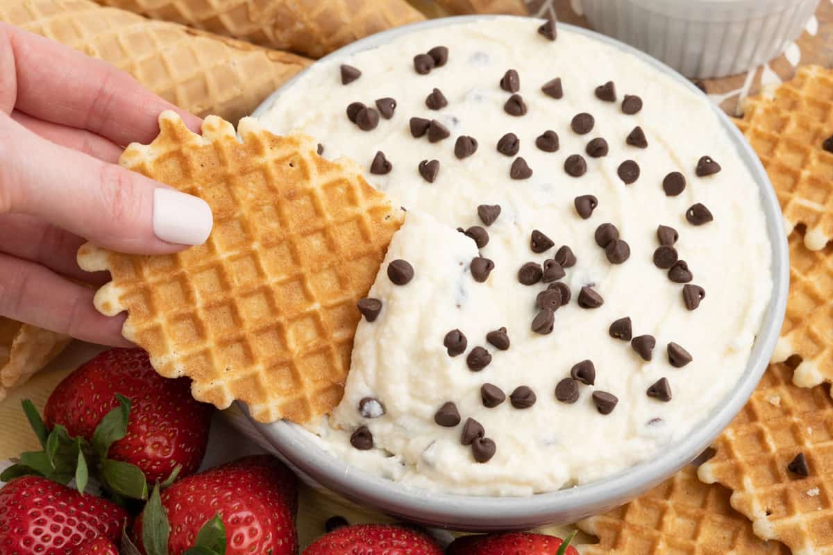 Waffle cookie being dipped into creamy ricotta and mascarpone cheese dip topped with chocolate chips.