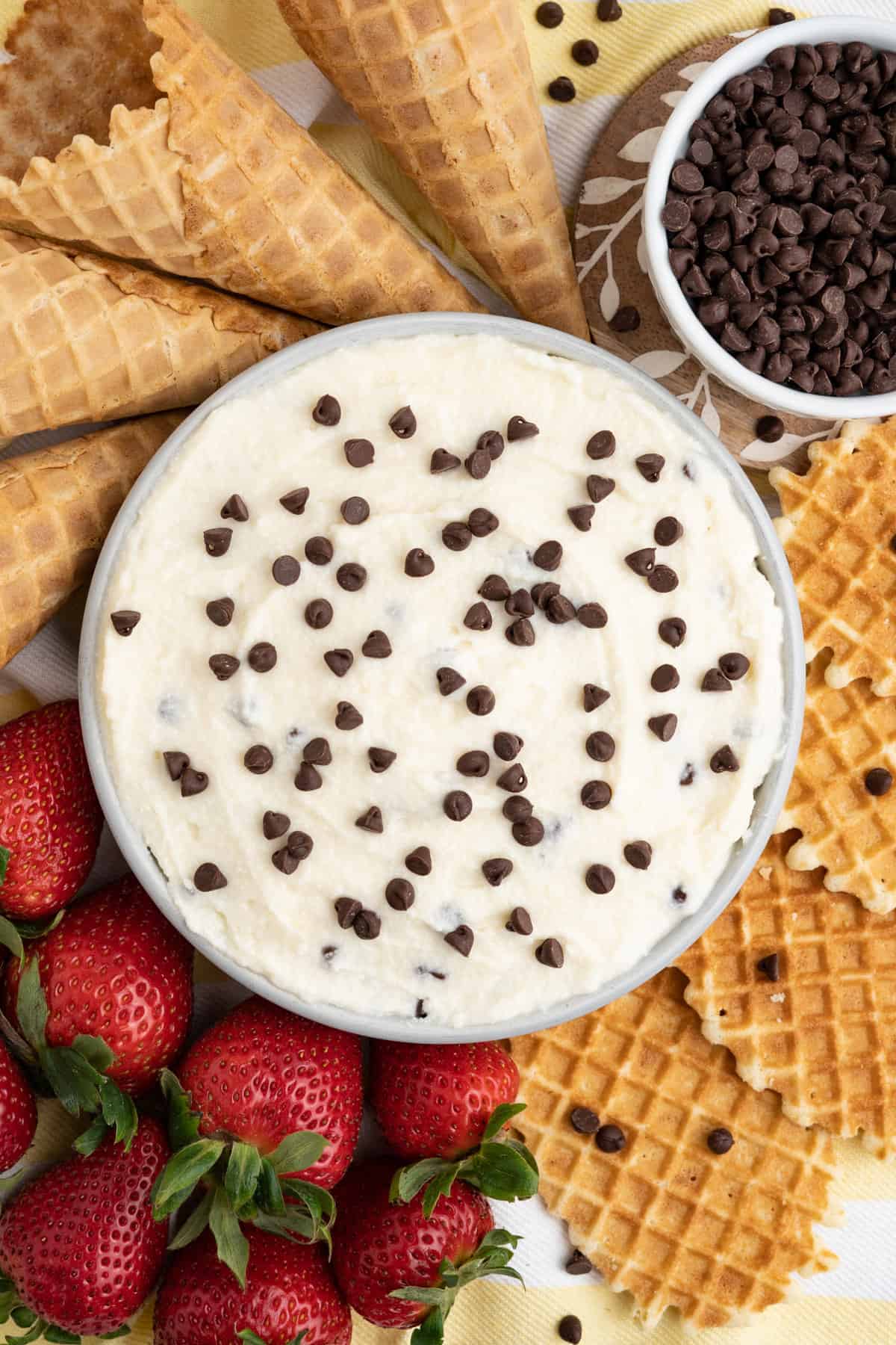 Creamy cannoli dip topped with mini chocolate chips and served with waffle cookies, ice cream cone pieces, and strawberries.