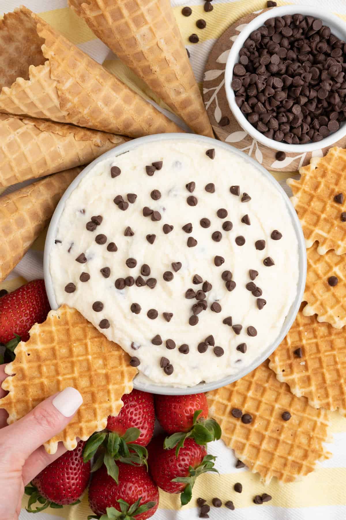 Hand reaching to dip waffle cookie into cannoli dip.