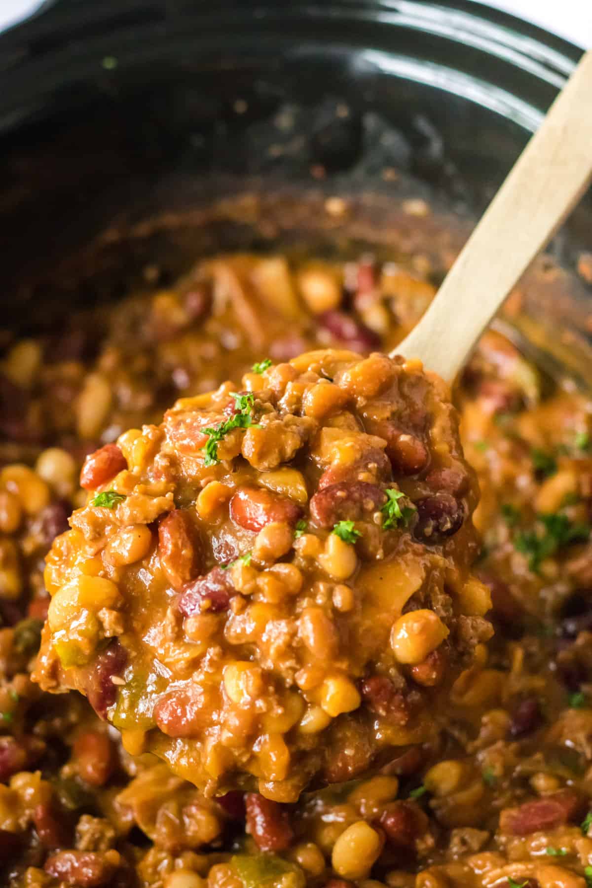 Wooden spoon lifting cowboy beans out from crockpot.