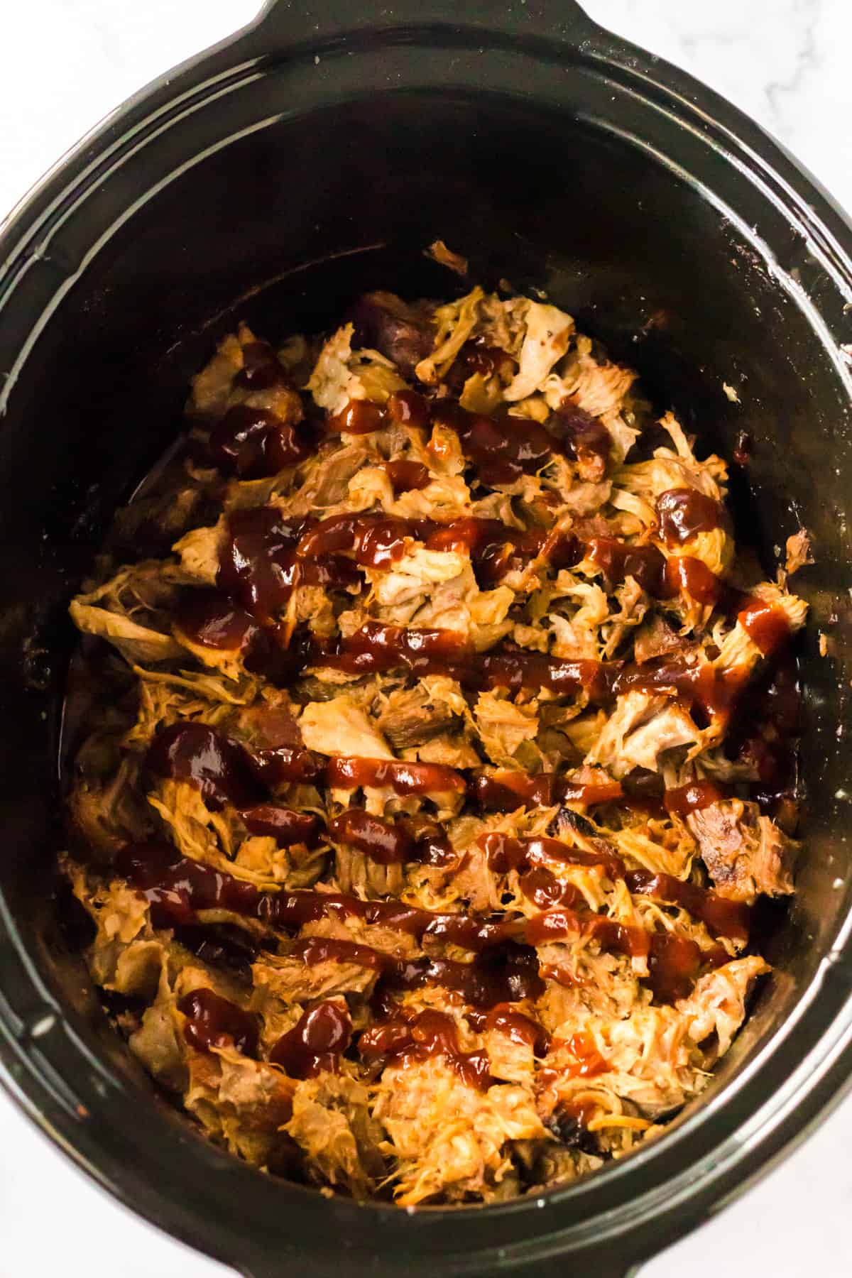 Root beer pulled pork with BBQ sauce drizzled over the top in the slow cooker.