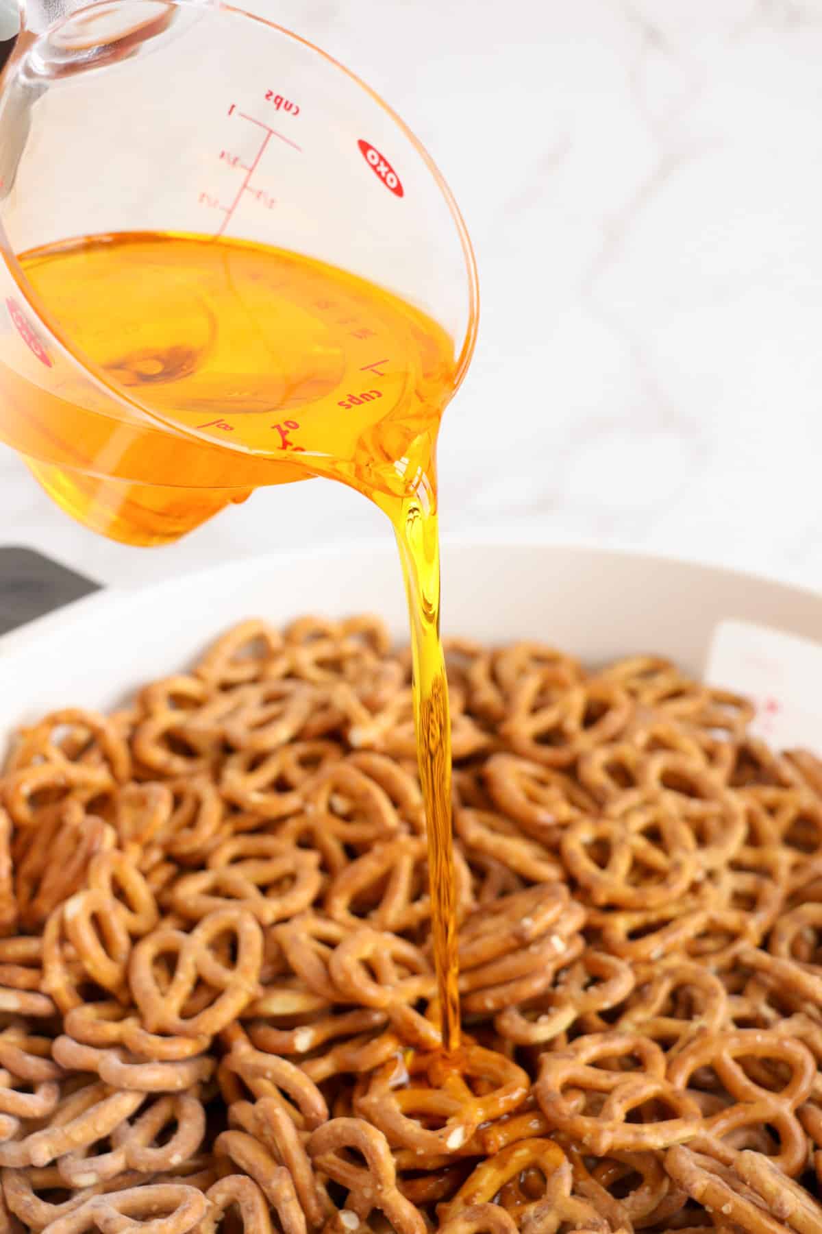 Popcorn oil being poured into bowl of pretzels.