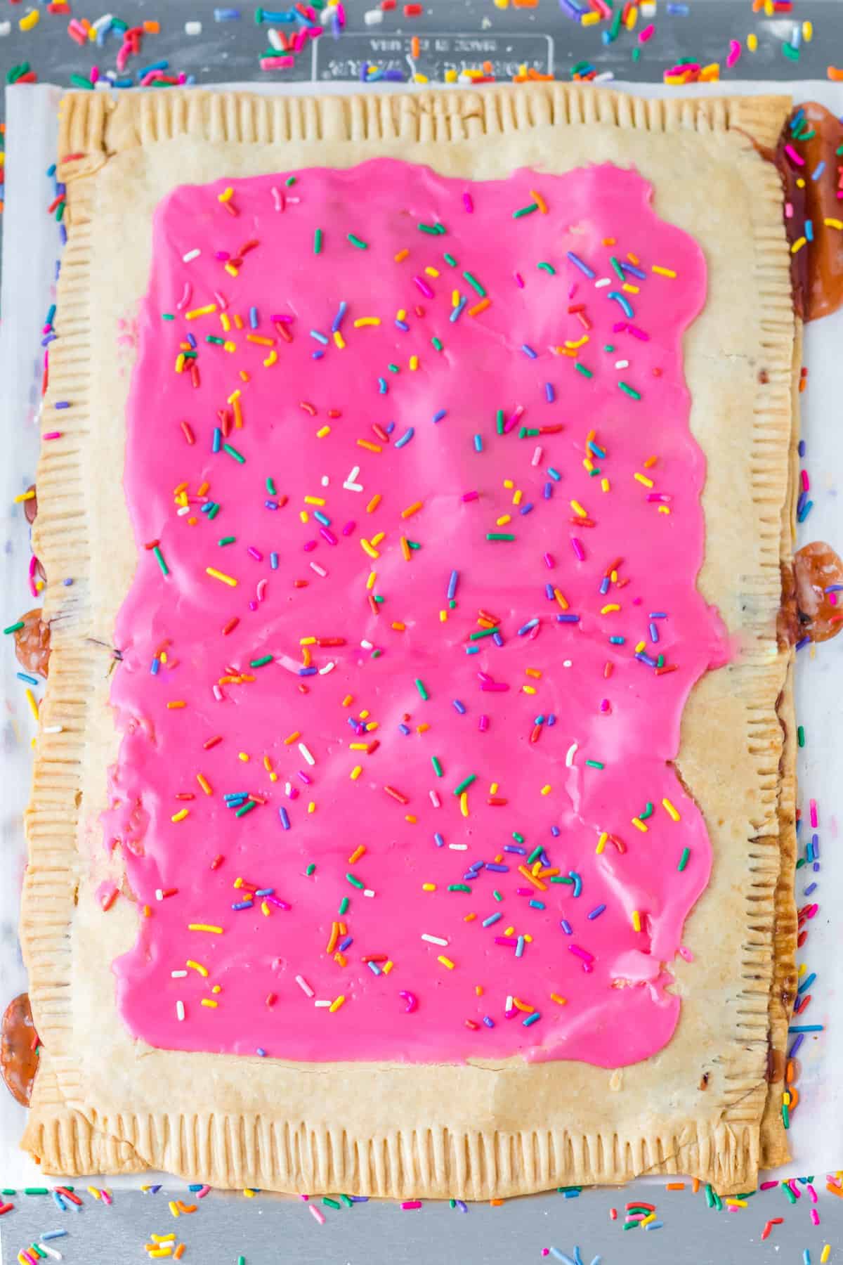 Giant strawberry pop tart with pink frosting and sprinkles on parchment lined sheet pan.