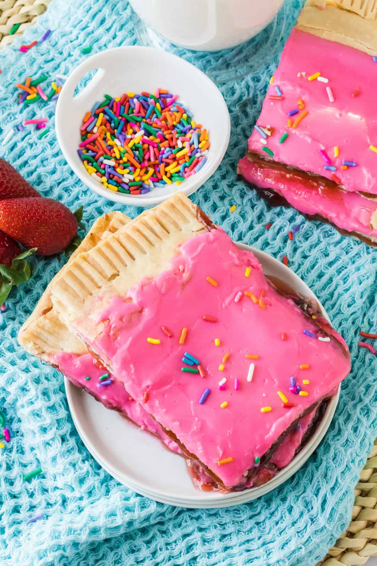 Two large pieces of a giant homemade pop tart on a plate with additional pieces and  sprinkles in the background.
