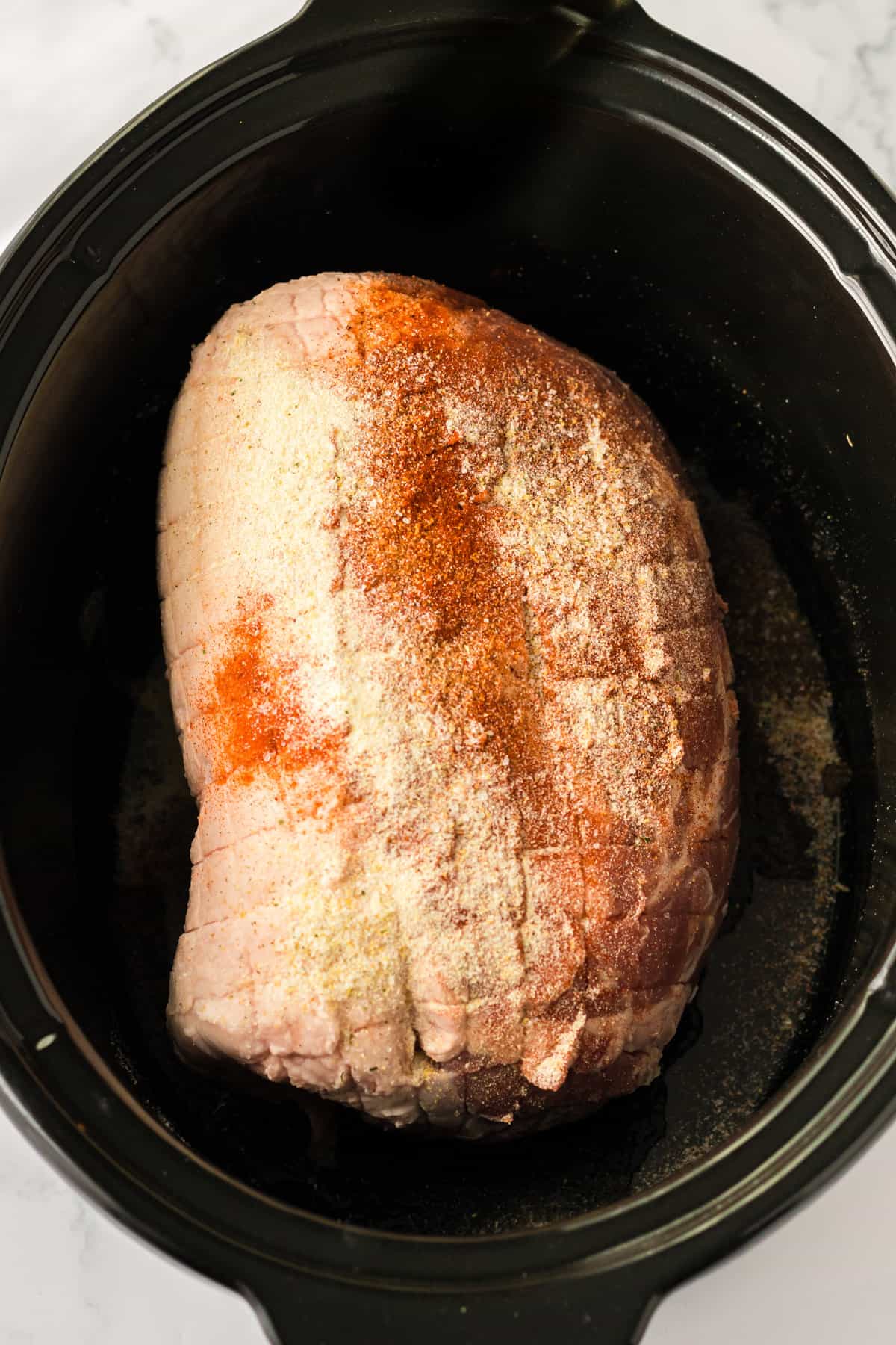 Pork shoulder butt roast in crockpot topped with seasonings.