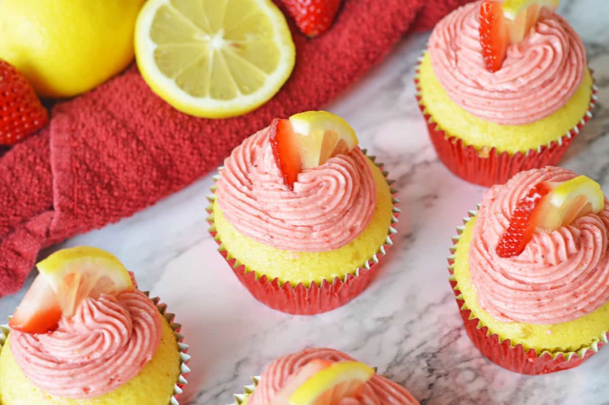 Lemon cupcakes with strawberry frosting and slice of lemon and strawberry on top.