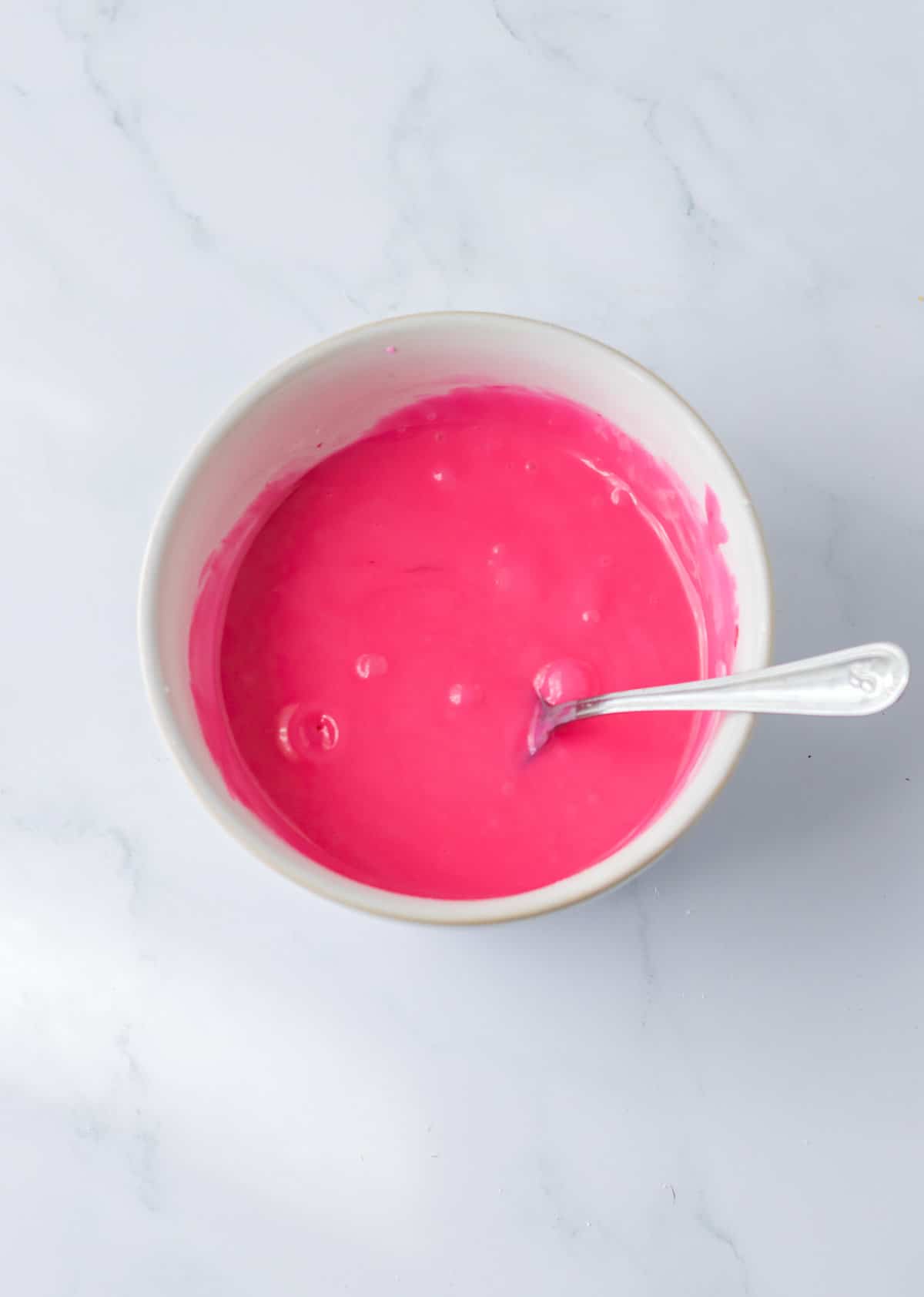 Pink icing in small bowl with spoon.