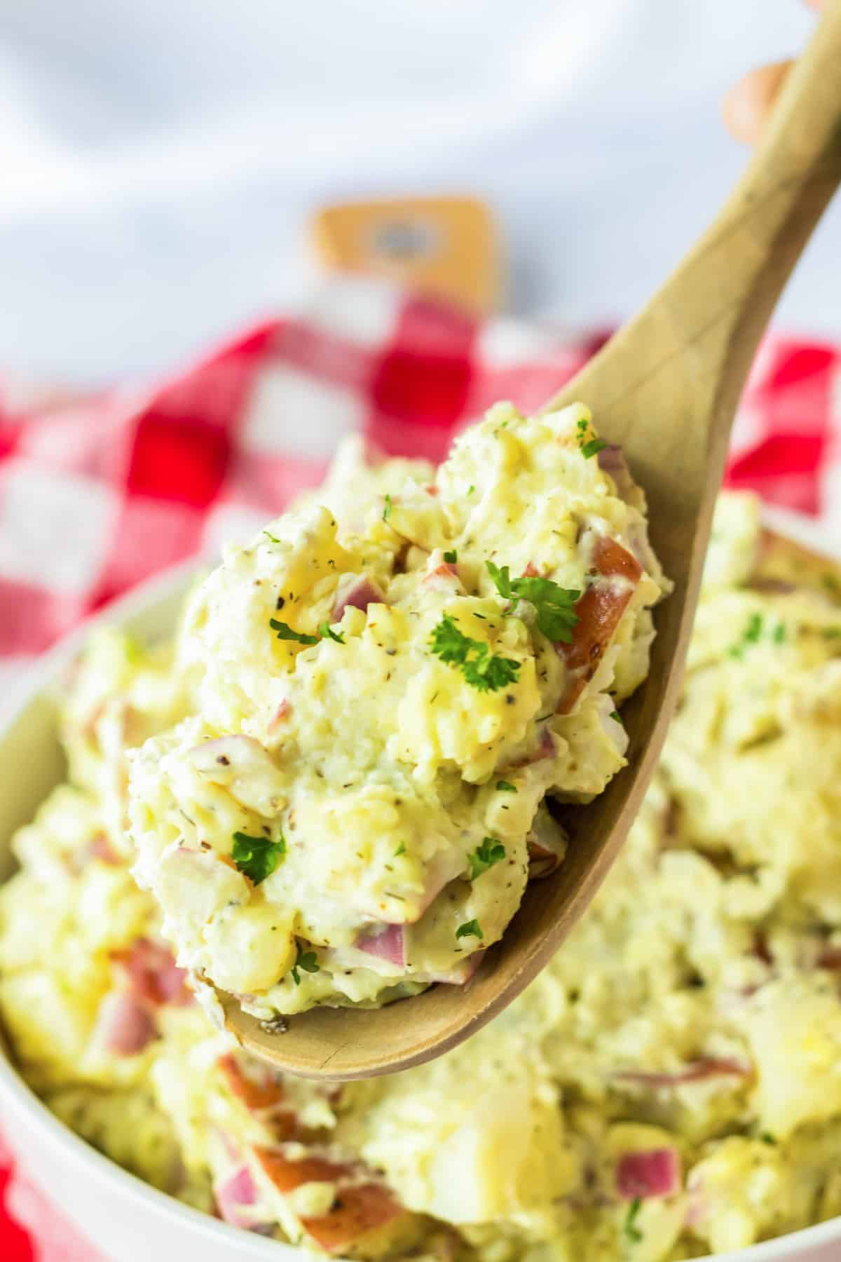 Red skin potato salad in a wooden spoon being lifted from bowl.