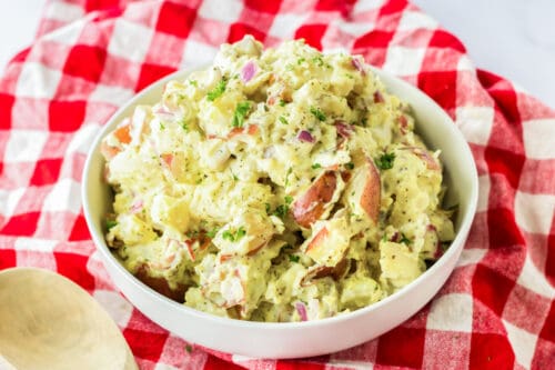 Old-fashioned red skin potato salad in white bowl on red plaid linen.