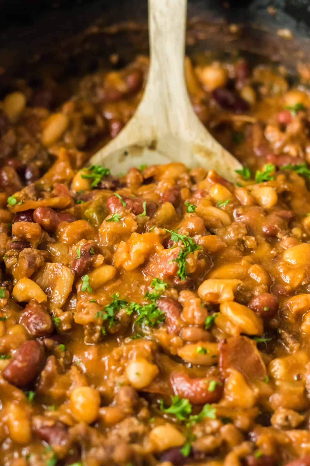 Cowboy beans in the slow cooker with wooden spoon.