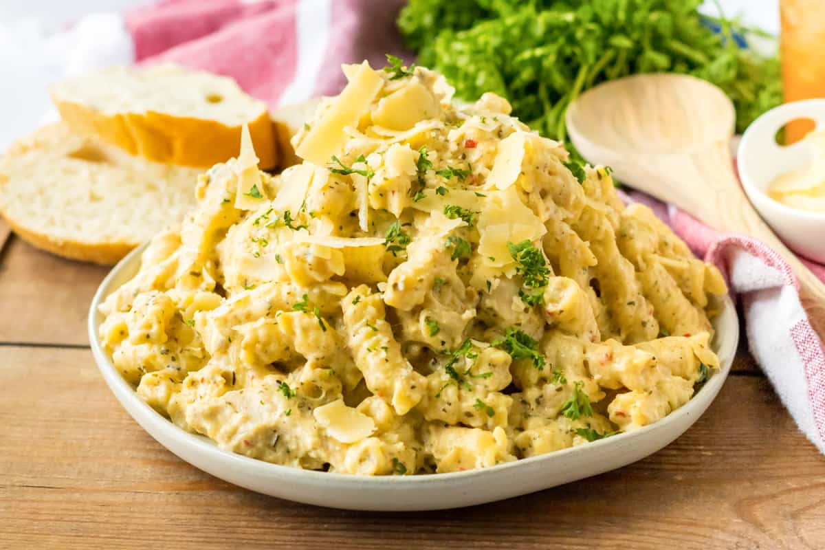 Crockpot parmesan garlic chicken pasta served on a white plate with fresh parsley and bread.