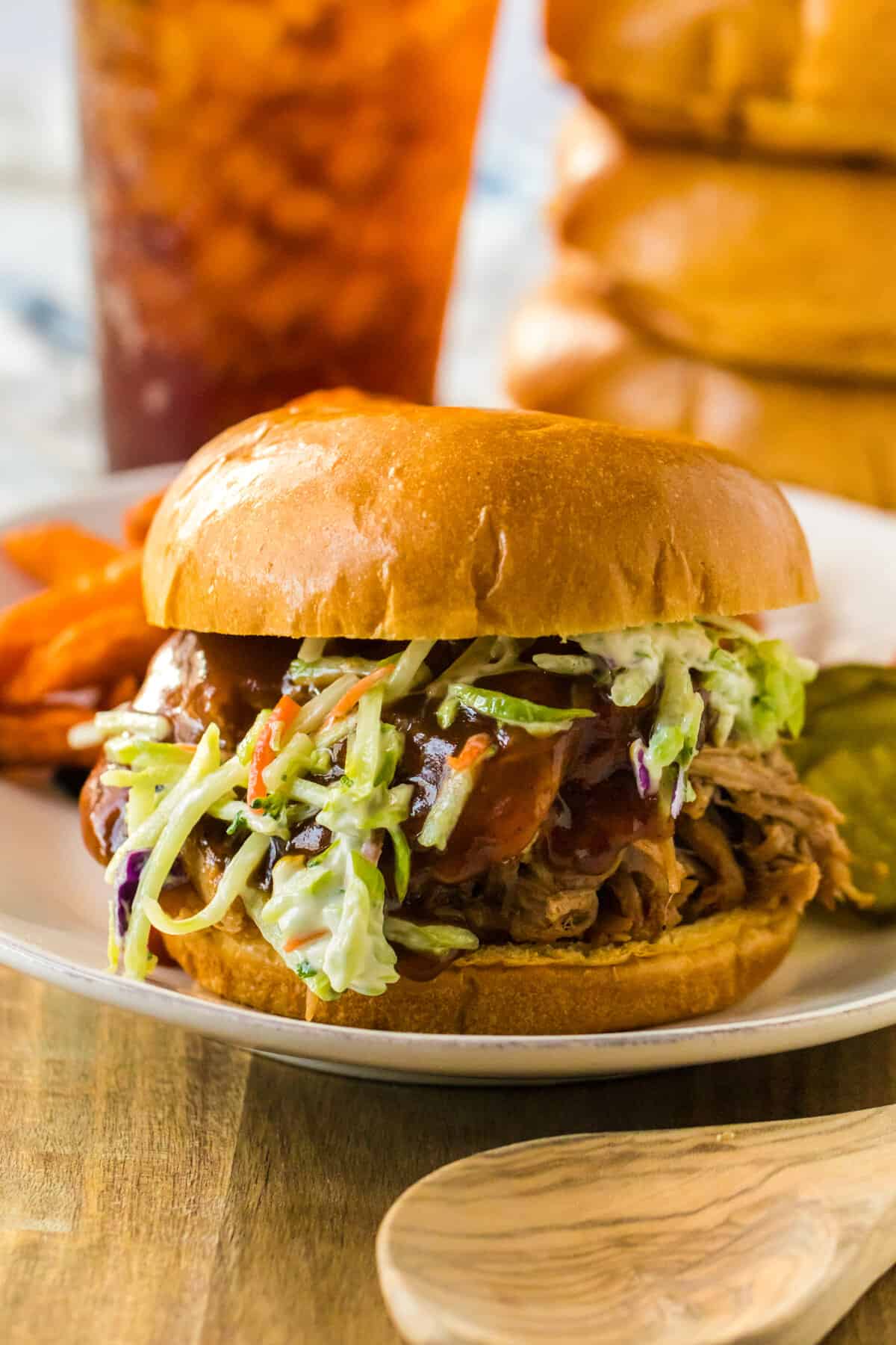 Root beer pulled pork sandwich topped with coleslaw and served with glass of iced tea and sweet potato fries.