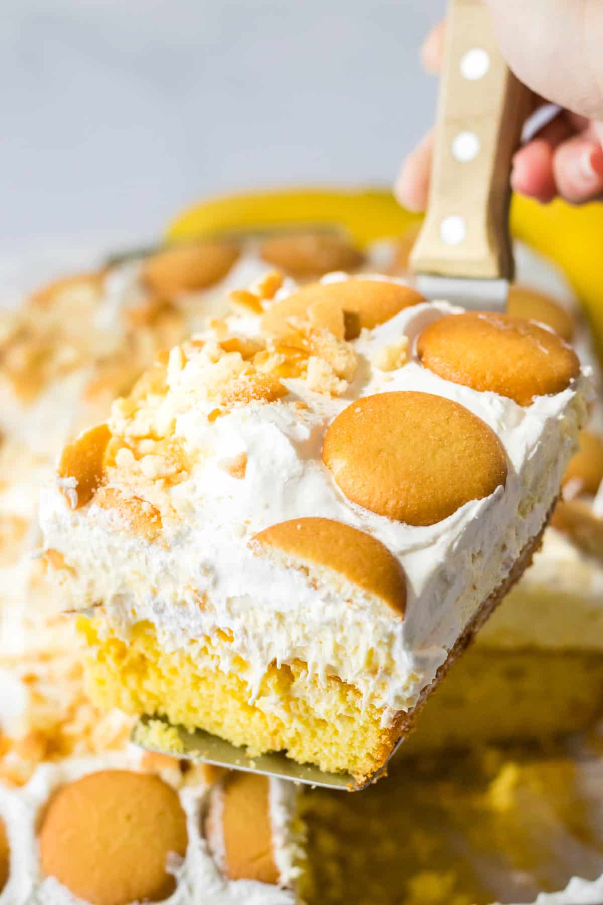 Slice of banana pudding poke cake being removed with a spatula.