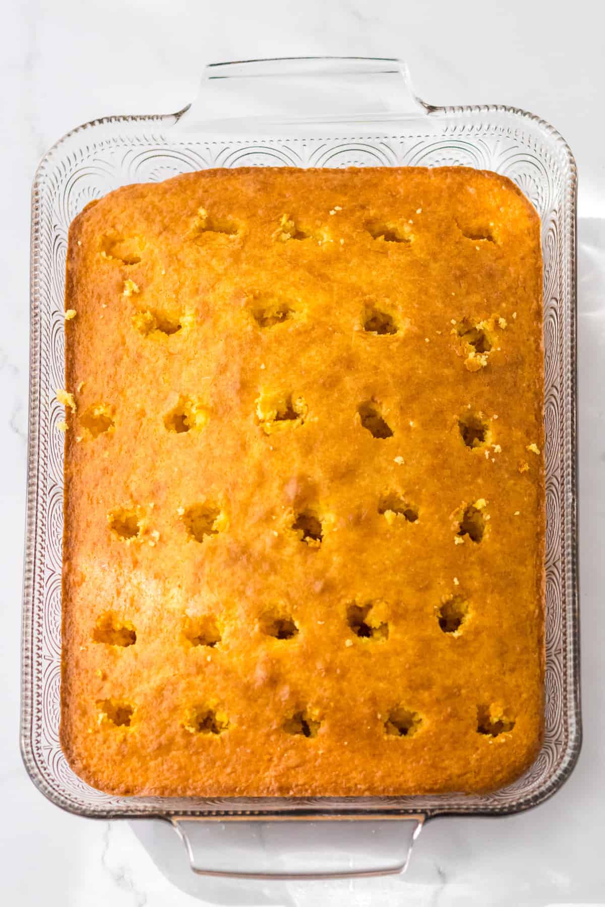 Rectangular yellow cake with holes poked throughout golden brown top.