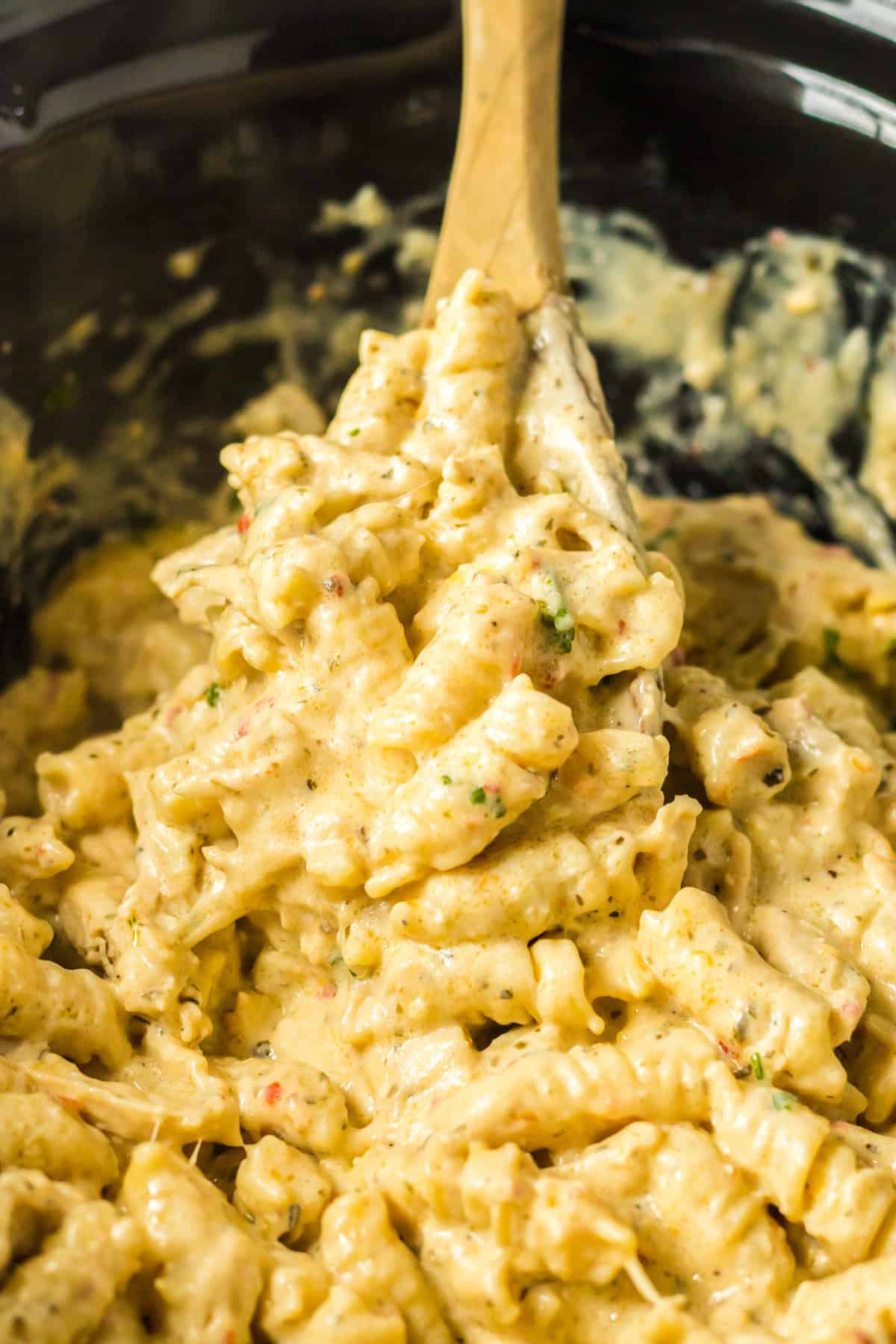 Crockpot parmesan garlic chicken pasta in bowl of a slow cooker with a wooden spoon stirring it.