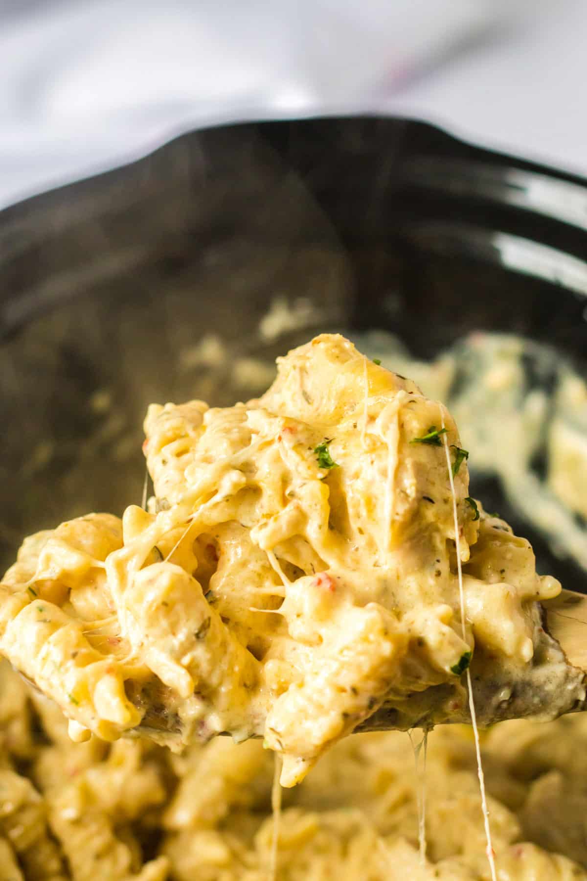 Spoon scooping steaming hot bww garlic parmesan chicken pasta out of crockpot.