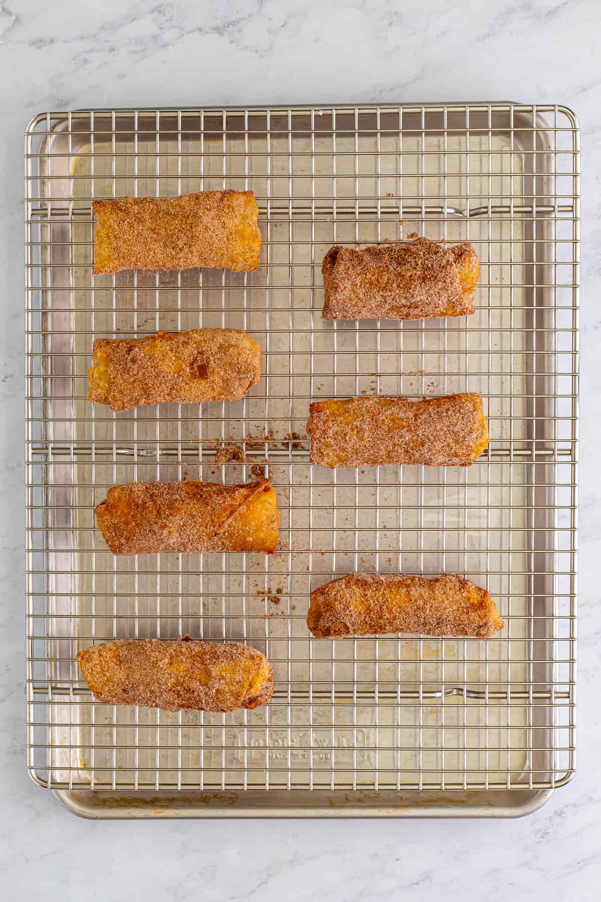 Cinnamon sugar coated egg rolls on baking sheet topped with wire rack.