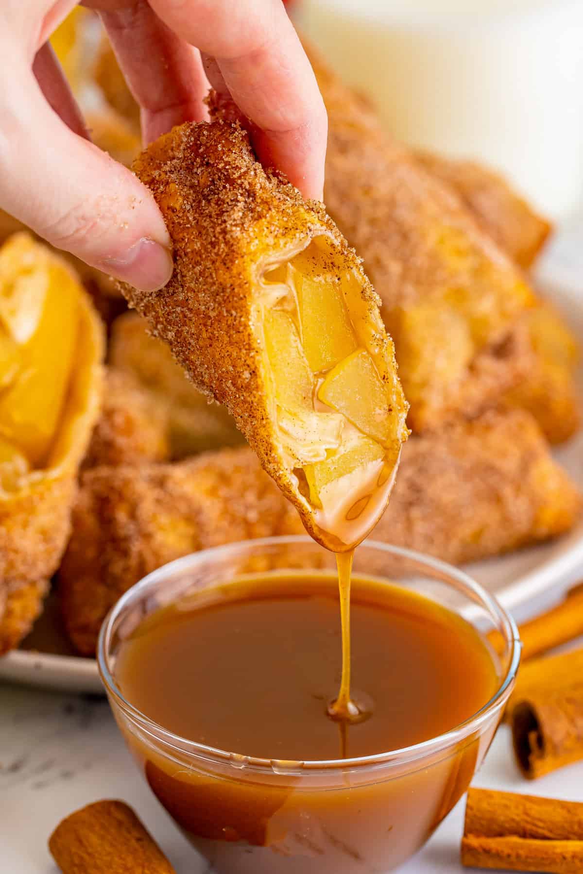 Apple pie egg roll being dipped in caramel sauce.