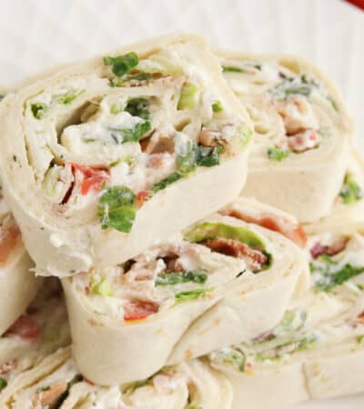 Ranch BLT Pinwheels made with flour tortillas, bacon, lettuce, tomatoes, and ranch dressing stacked on a white plate.