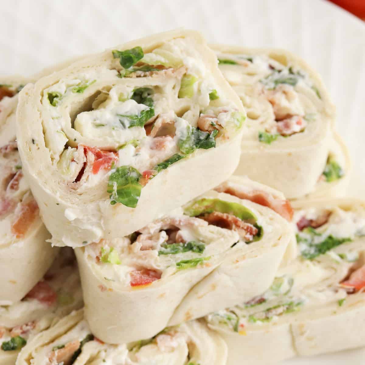 Ranch BLT Pinwheels made with flour tortillas, bacon, lettuce, tomatoes, and ranch dressing stacked on a white plate.