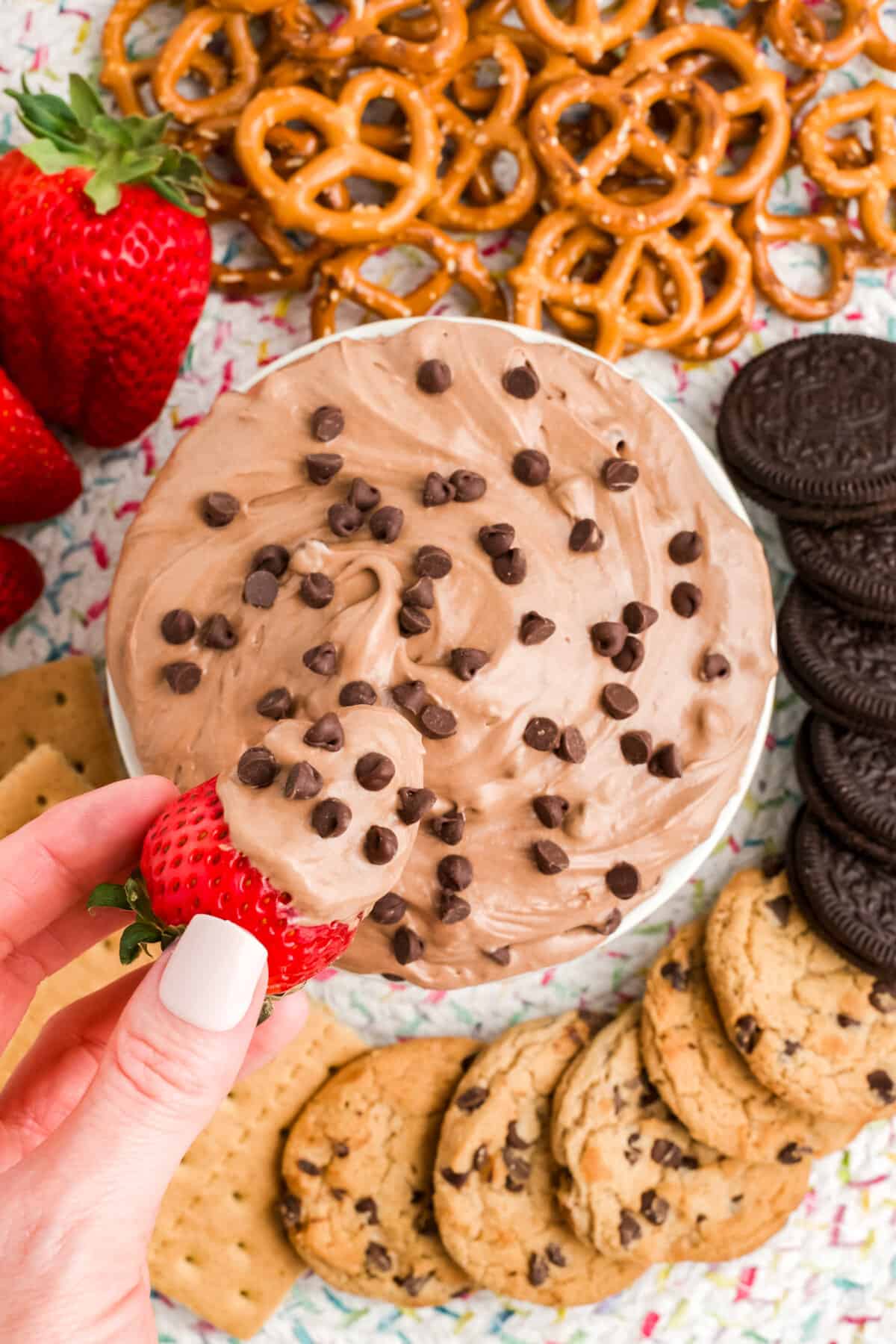 Hand dipping fresh strawberry in brownie batter dip.
