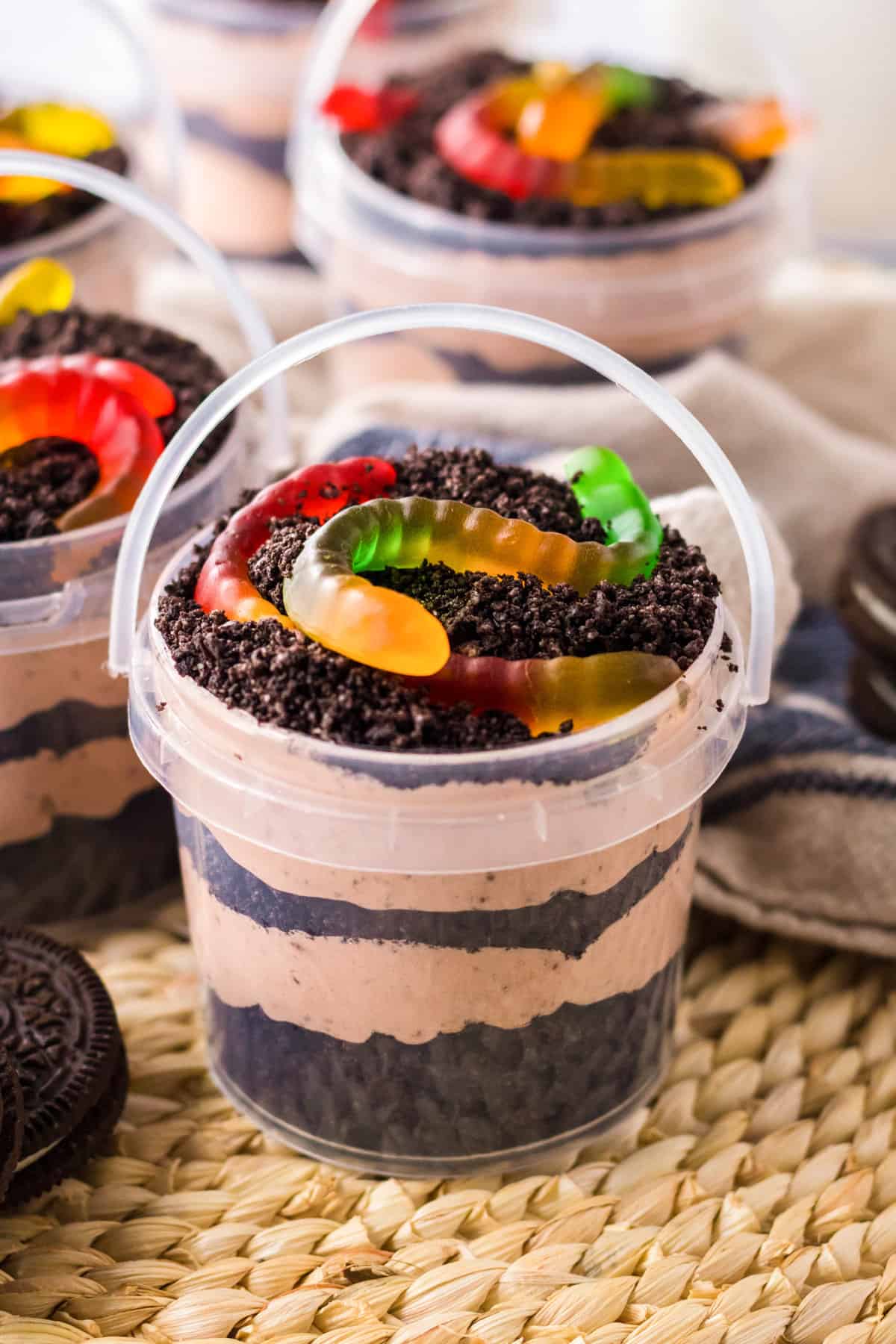 Dirt and worms pudding cups in clear pails with layers of creamy chocolate pudding and crushed oreo pieces.