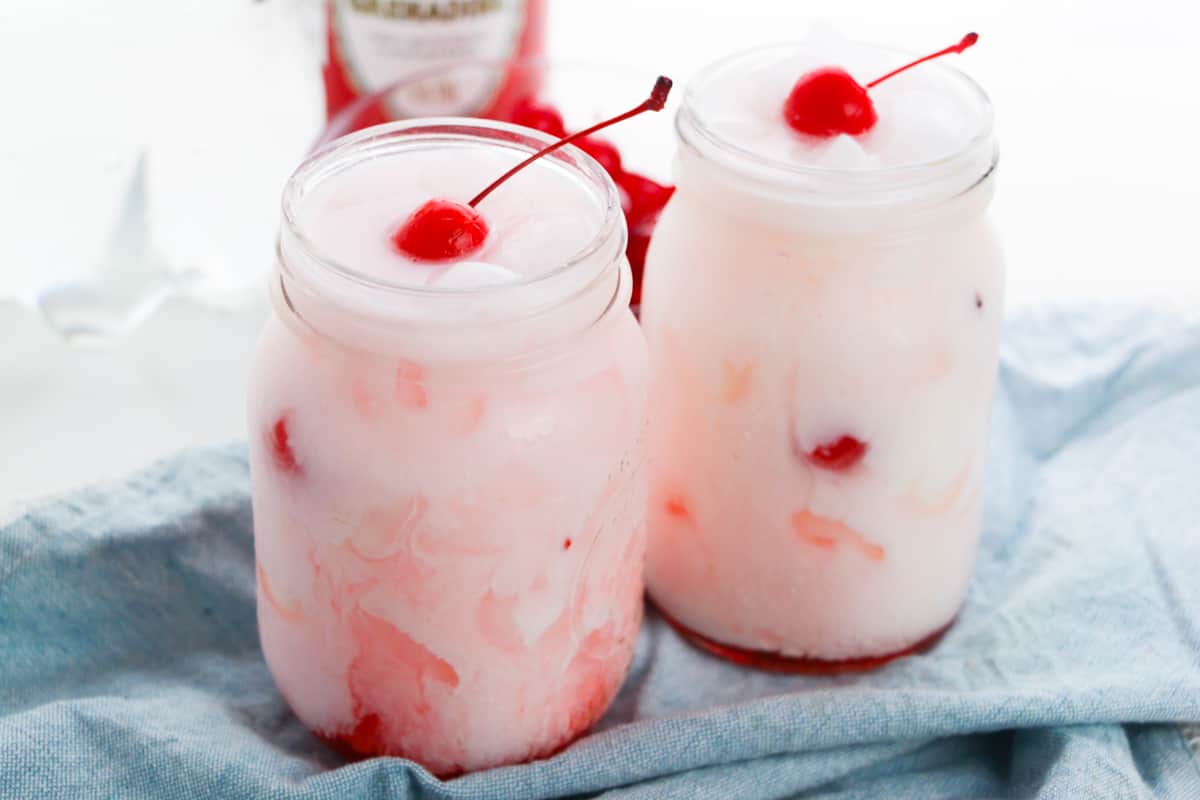Shirley temple dirty sodas garnished with cherries in two mason jars.
