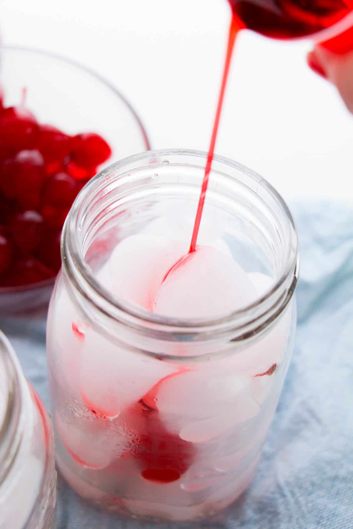 Grenadine being poured into ice-filled mason jar.
