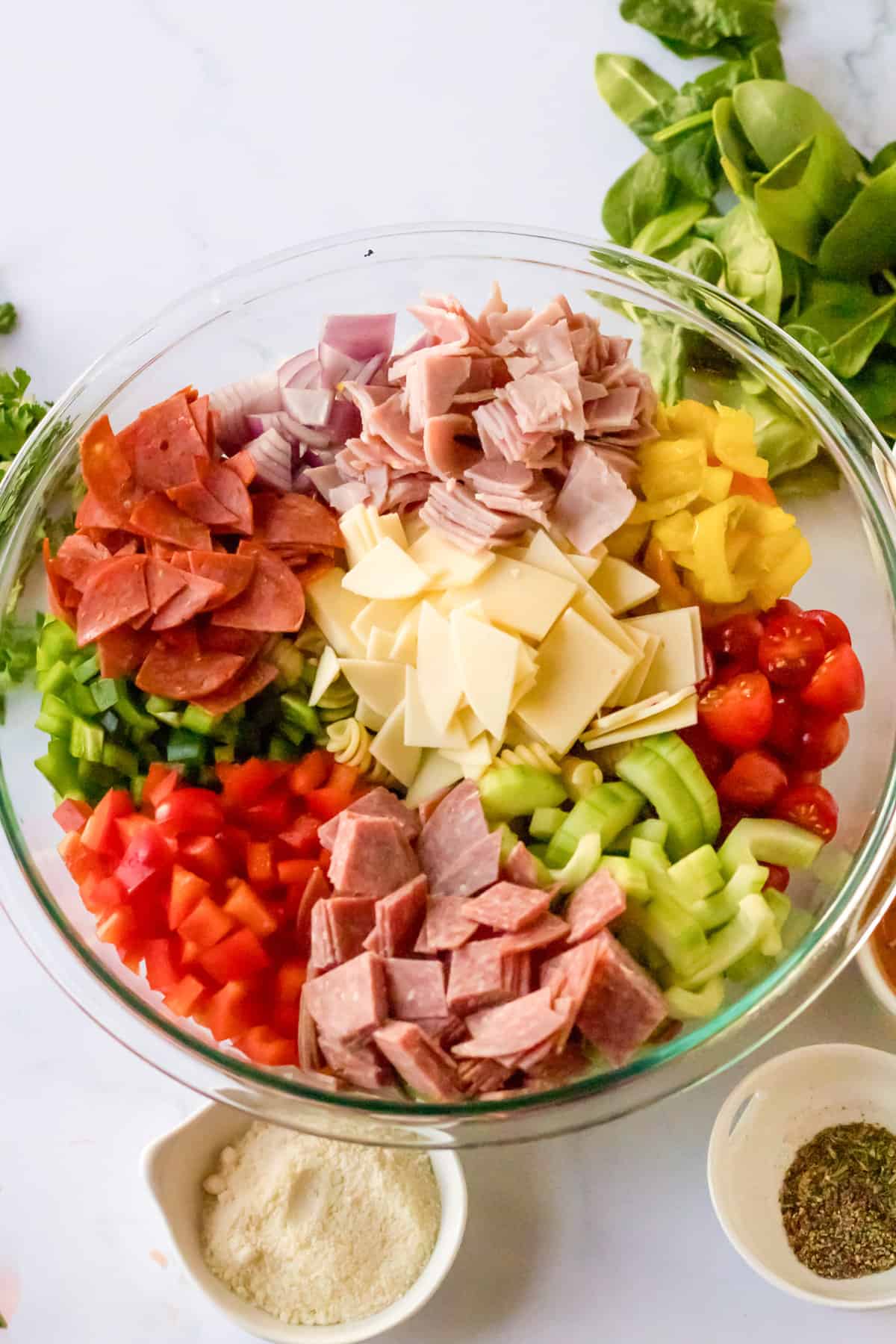 Glass bowl with chopped deli meat, cheese, and veggies.