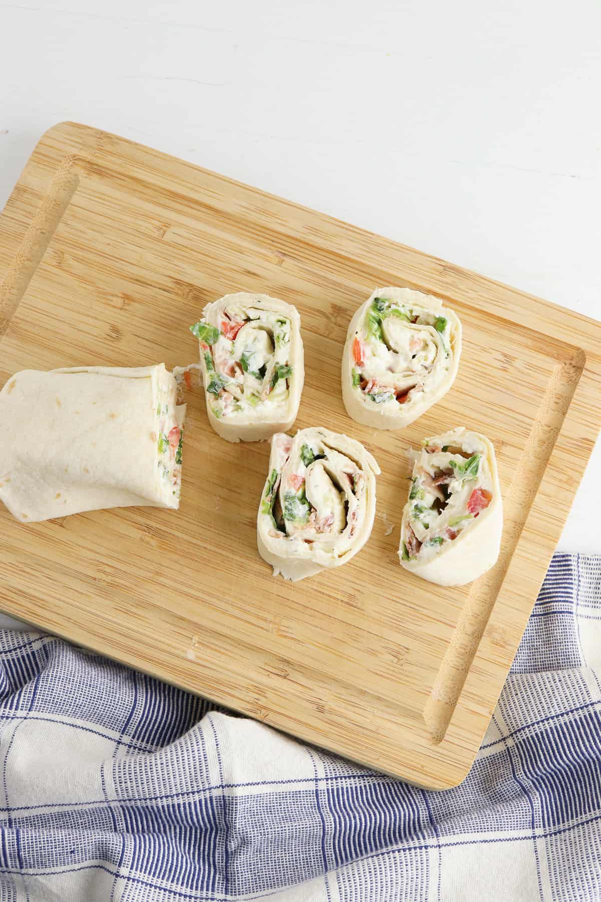 Rolled up tortilla being cut into1-inch slices on a wooden cutting board.