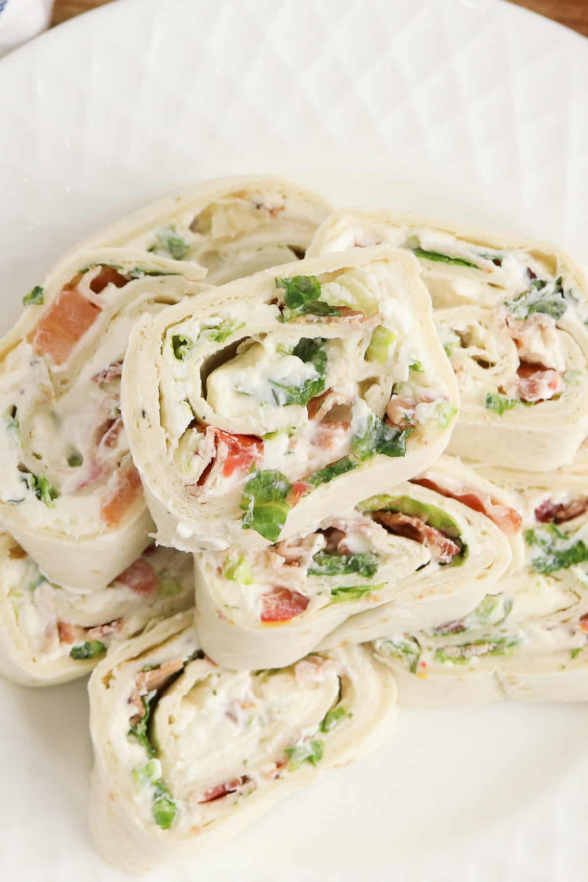 Overhead photo of ranch blt pinwheels stacked on top of one another and served on a white plate.