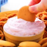 Bowl of raspberry cream cheese dip with vanilla cookie being dipped in it.