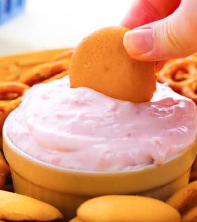 Bowl of raspberry cream cheese dip with vanilla cookie being dipped in it.