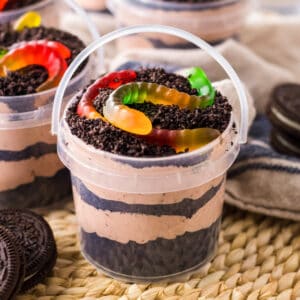 Dirt and worms pudding cups in clear pails with layers of creamy chocolate pudding and crushed oreo pieces.