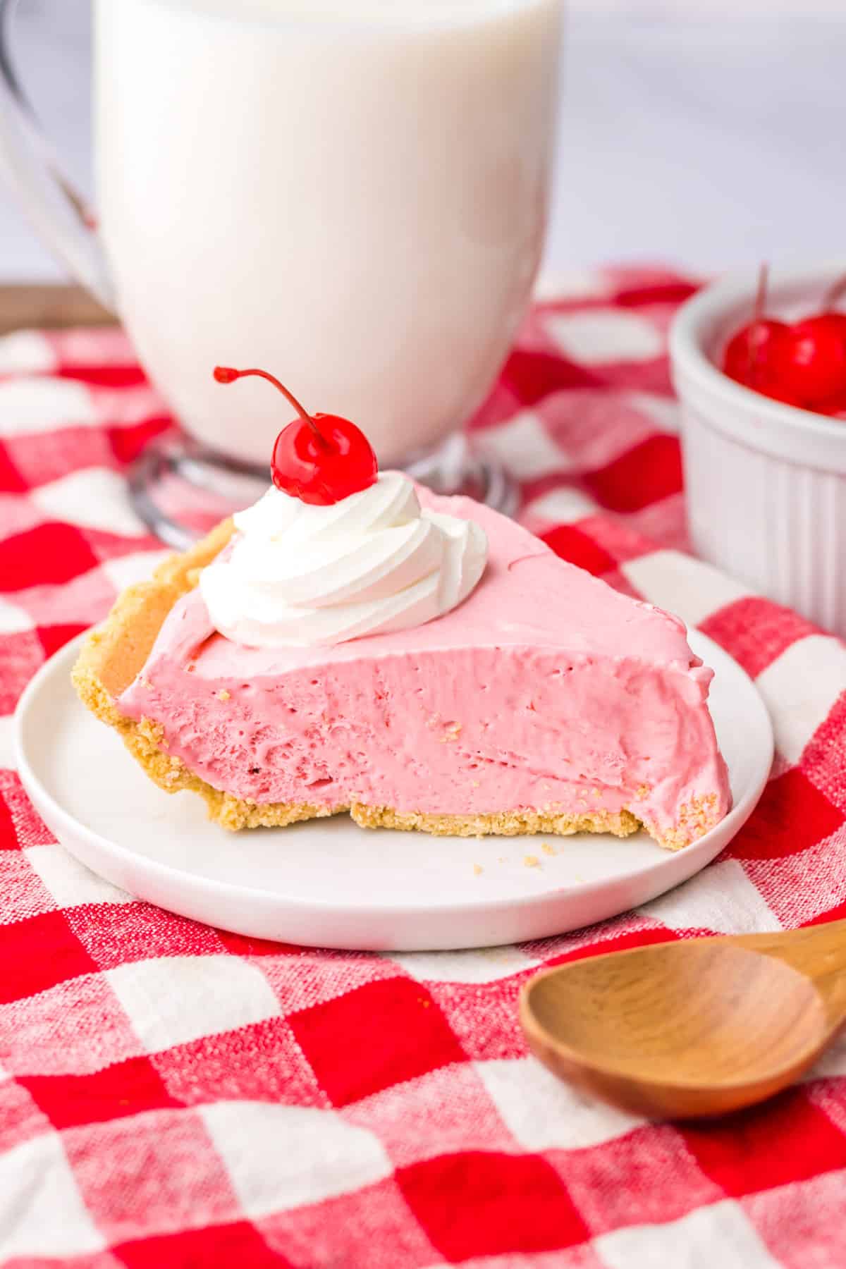 Slice of cherry cool aid pie on white plate with large glass of milk in the background.