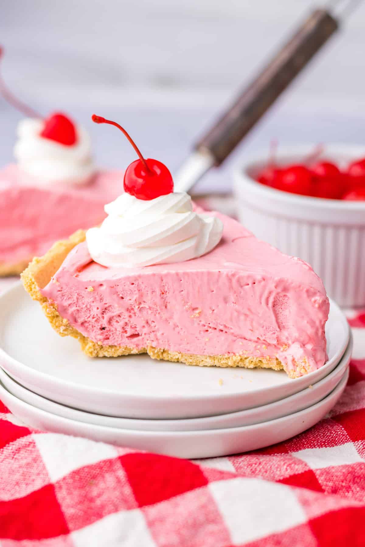 Slice of no bake kool aid pie with cool whip and cherry on top.