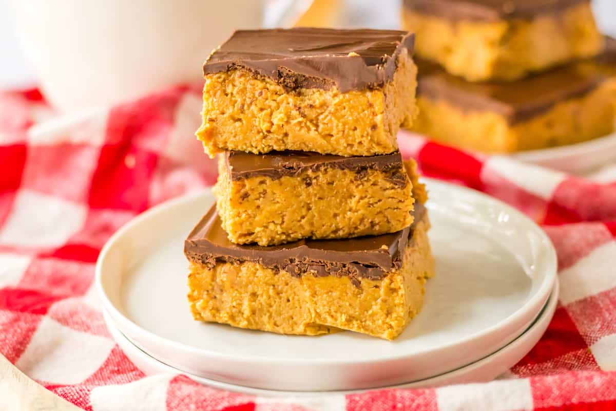 5 Ingredient no-bake chocolate peanut butter bars stacked on top of one another on white plate with milk and more no bake bars in the background.