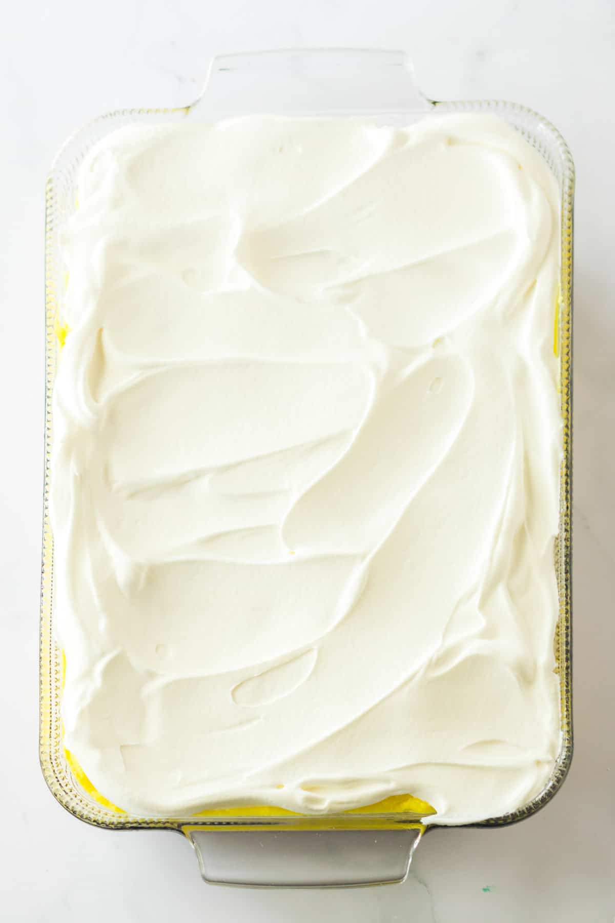 Whipped topping spread into an even layer in a rectangular glass dish.