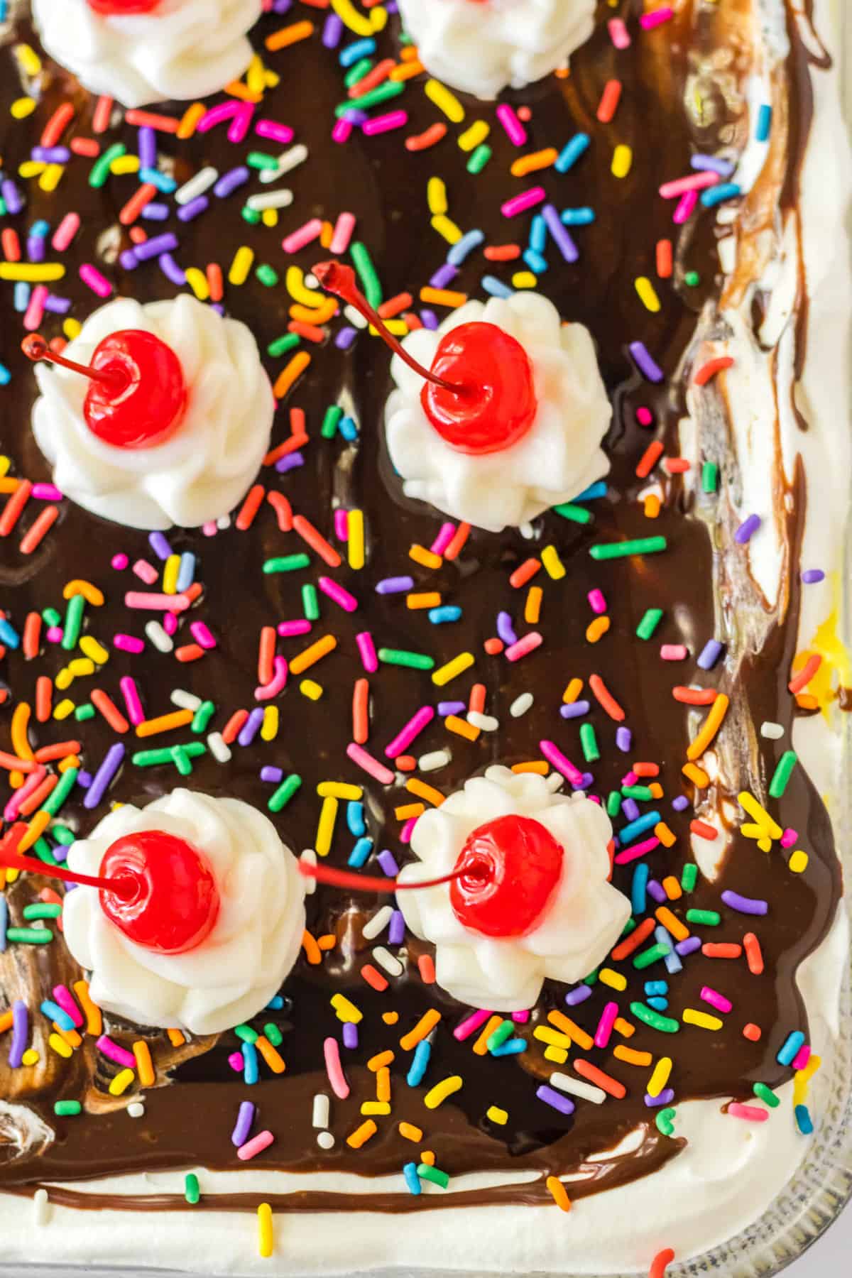 Banana split lush dessert with chocolate sauce, sprinkles, whipped cream, and cherries on top.