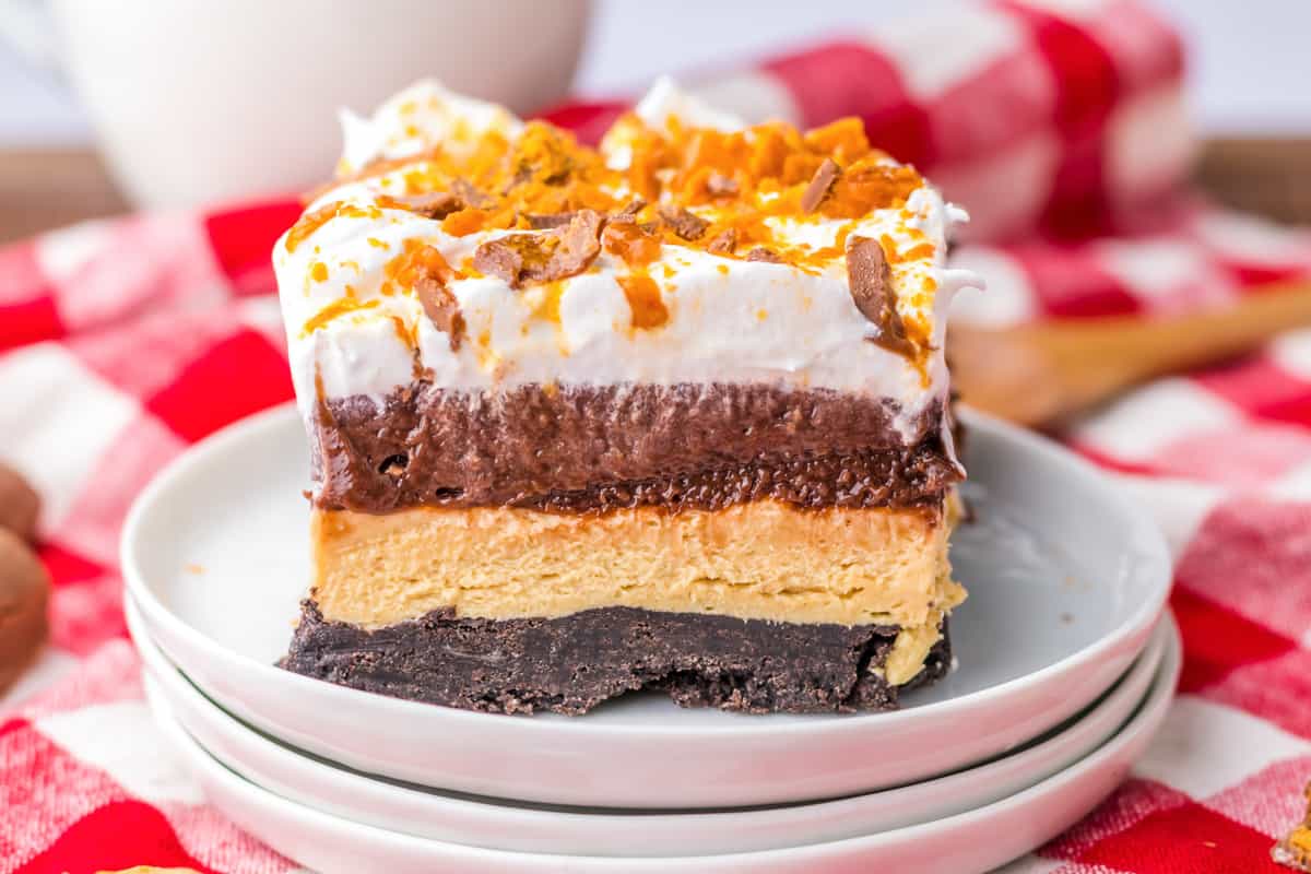 Butterfinger lush with an oreo cookie crust and layers of no bake peanut butter cheesecake, chocolate pudding, cool whip, and crushed butterfingers.