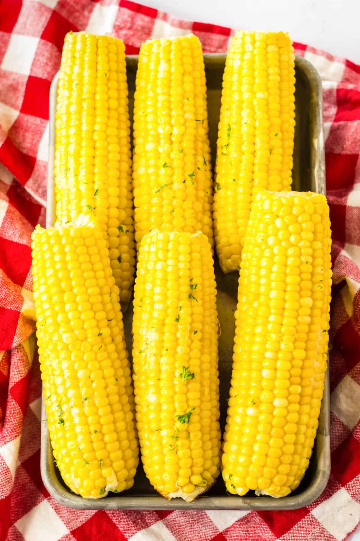 Slow cooked corn on the cob served on a metal tray.