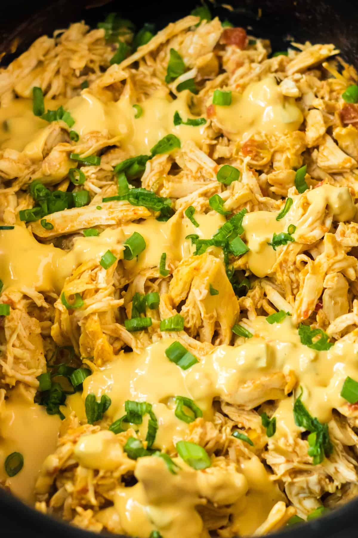 Cheesy shredded chicken in the crockpot topped with queso and chopped green onions.